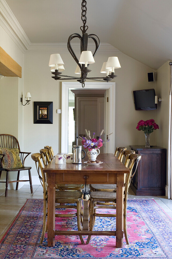 Wooden dining table and chairs below chandelier in Surrey home UK