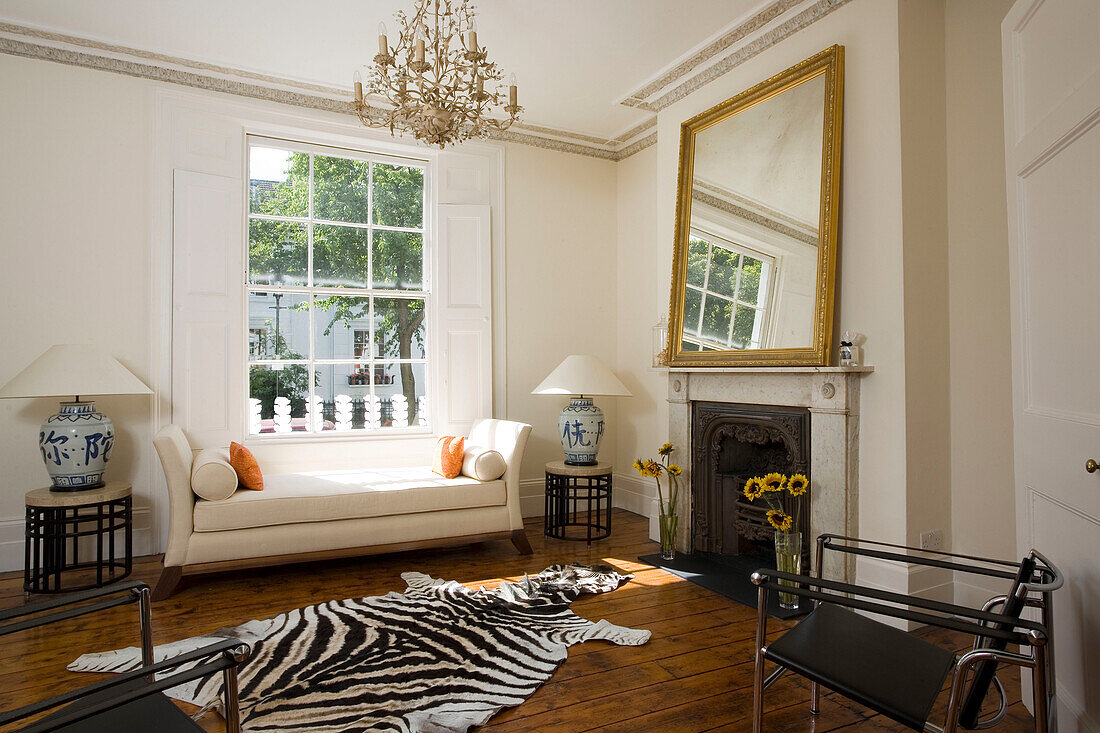Sofa at sunlit window of townhouse with zebra print rug and gilt mirror on fireplace