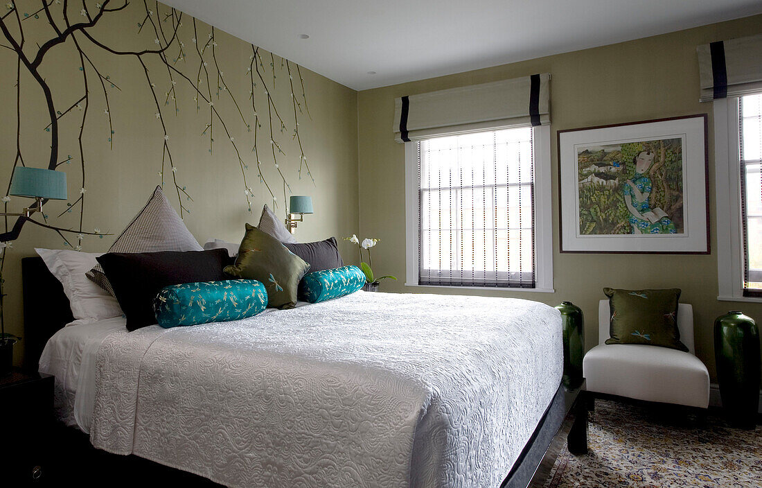 Oriental wall decor in bedroom with white quilted bed cover and upholstered cushions in contemporary London townhouse, England, UK