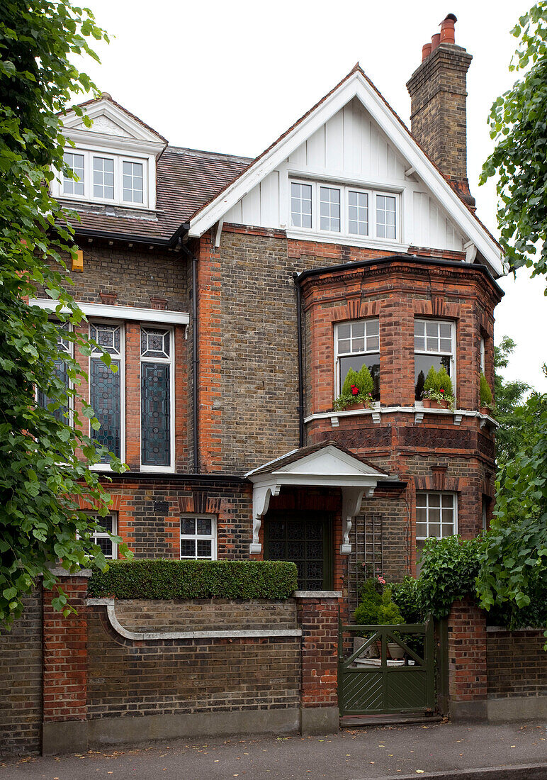 Brick exterior of semi-detached house with pitched roof and porch and bay windows, London, UK