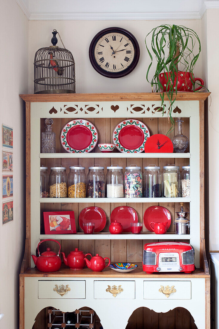 Birdcage on kitchen dresser with red crockery and storage jars in London townhouse, England, UK