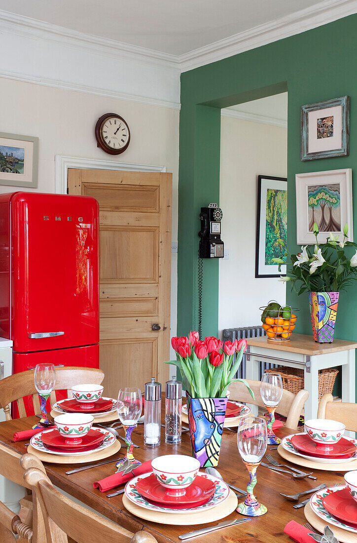 Bright orange upright fridge in green kitchen with set table in London townhouse, England, UK