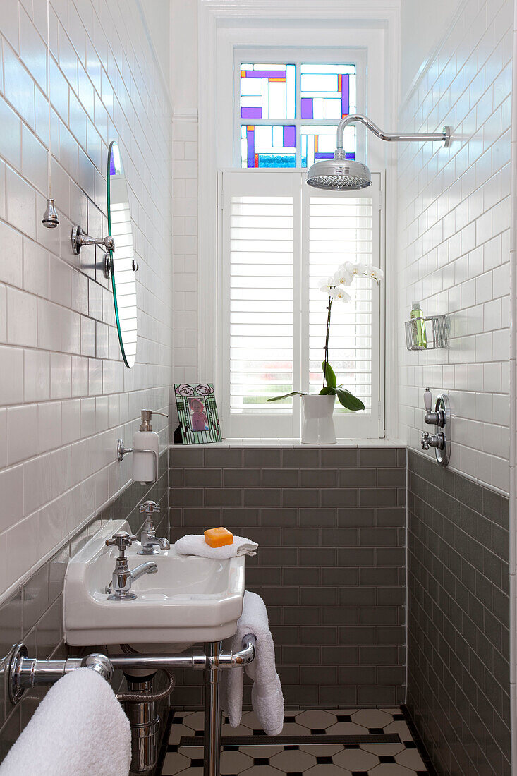 Duscharmatur und Waschtisch in einem grau gefliesten schmalen Badezimmer in einem Londoner Stadthaus, England, UK