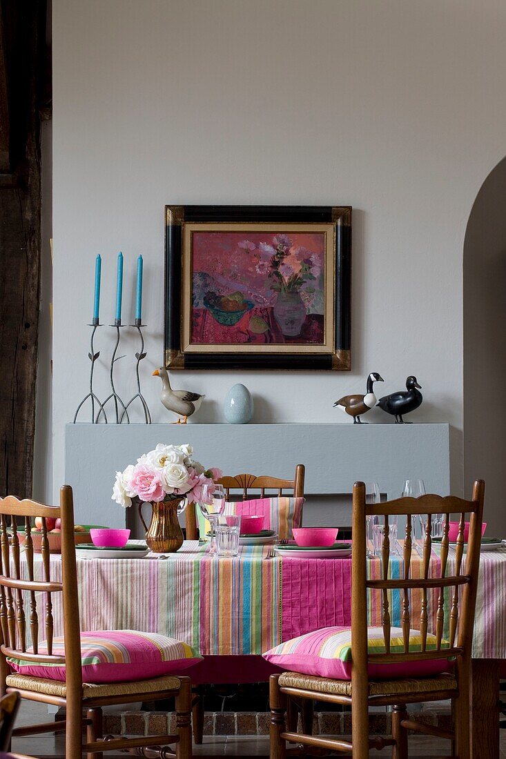 Artwork above fireplace in Sussex dining room with pink striped tablecloth