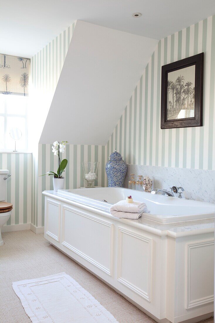 White bath tub under slanted ceiling with striped wallpaper in Kent cottage, England, UK