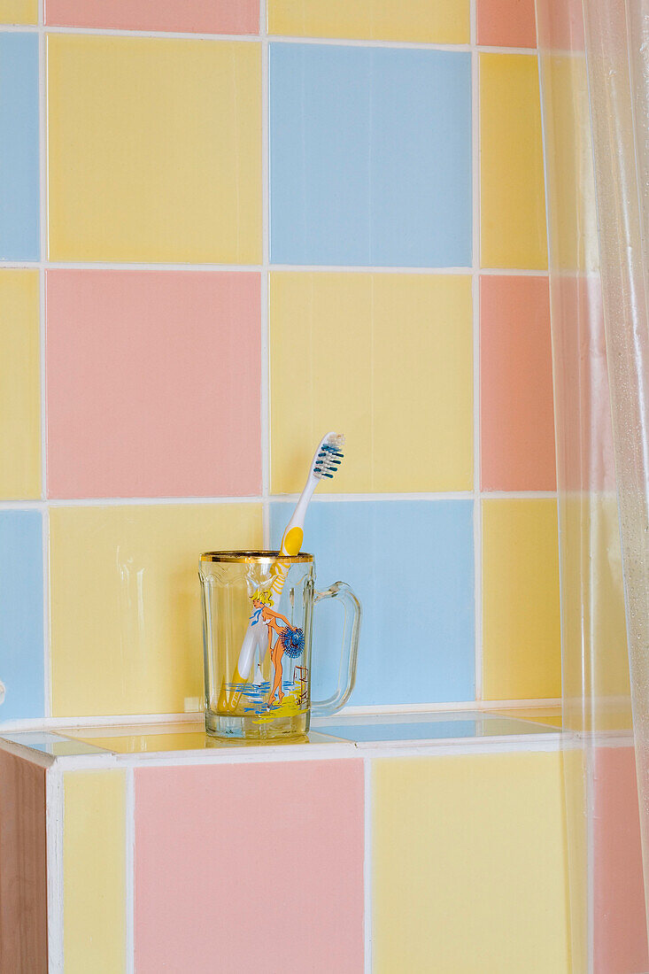 Zahnbürste in einem Glasbecher mit mehrfarbigen pastellfarbenen Fliesen im Badezimmer eines Hauses in Rye, East Sussex, England, UK