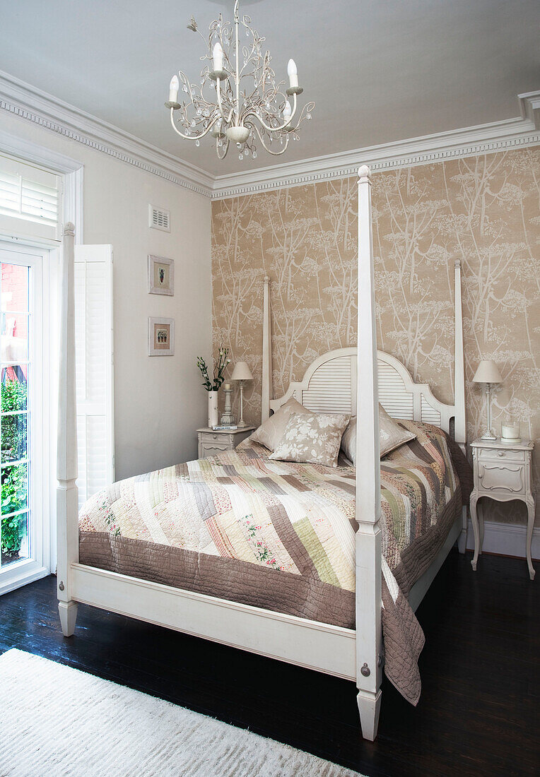 White painted for postered bed in bedroom with neutral floral patterned wallpaper, Surrey home, England, UK