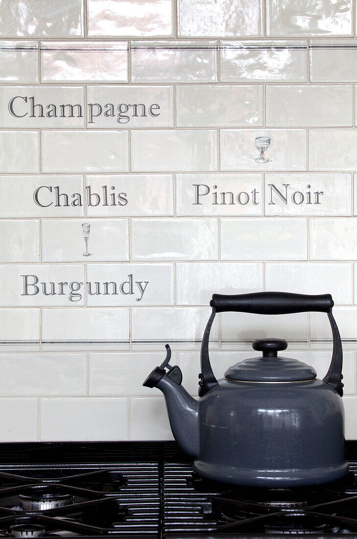 Grey kettle on gas hob with french lettering white tiled splashback in kitchen of Surrey home, England, UK