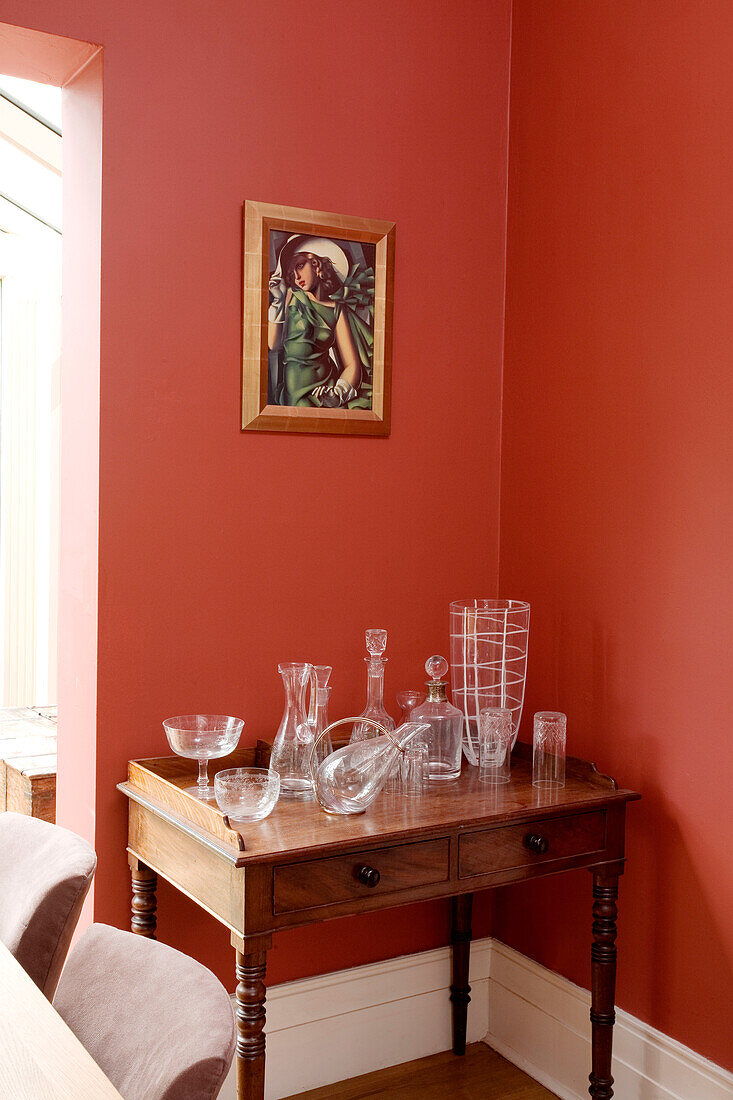 Glassware on wooden side table below artwork in London home, England, UK