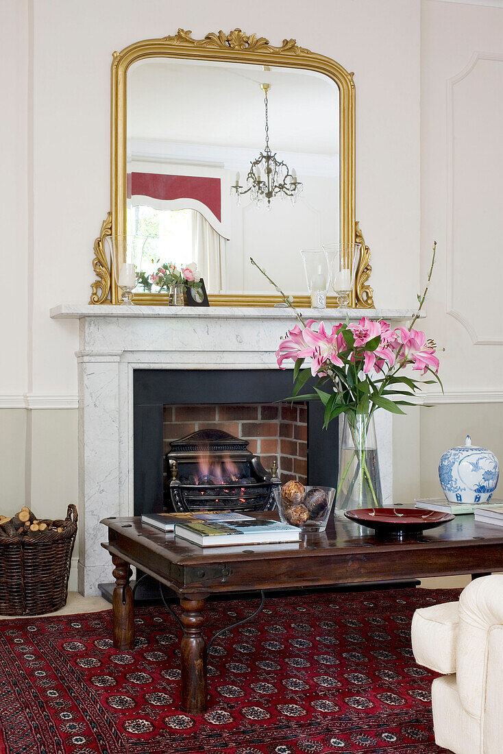 Cut lilies on wood coffee table with gilt mirror on mantlepiece in classic Tyne & Wear home, England, UK