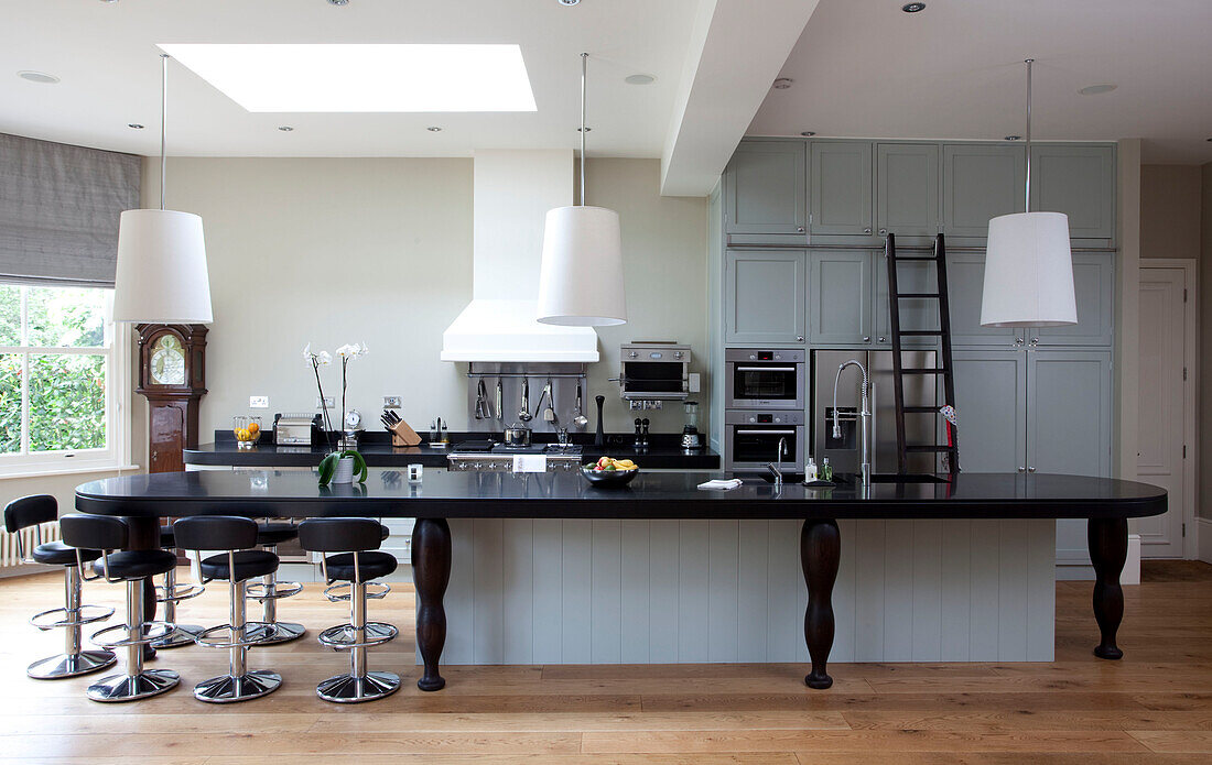 Pendant shades hang above extensive kitchen counter and breakfast bar in classic London home, UK