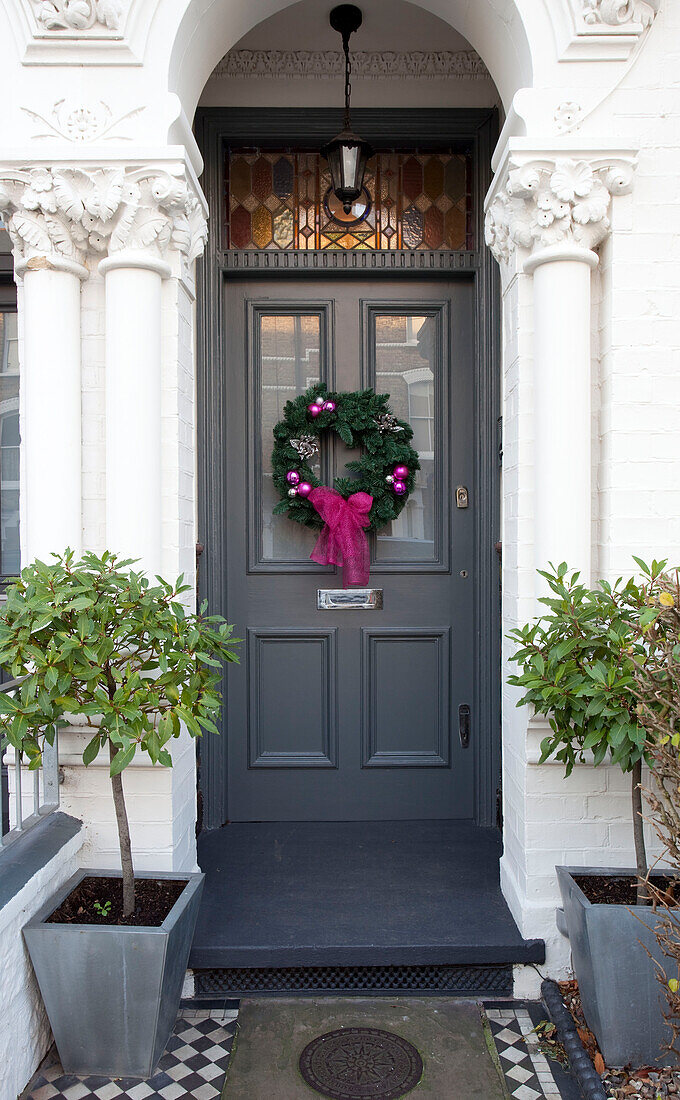 Blumenkranz mit rosa Schleife an der grauen Haustür eines Londoner Stadthauses, UK