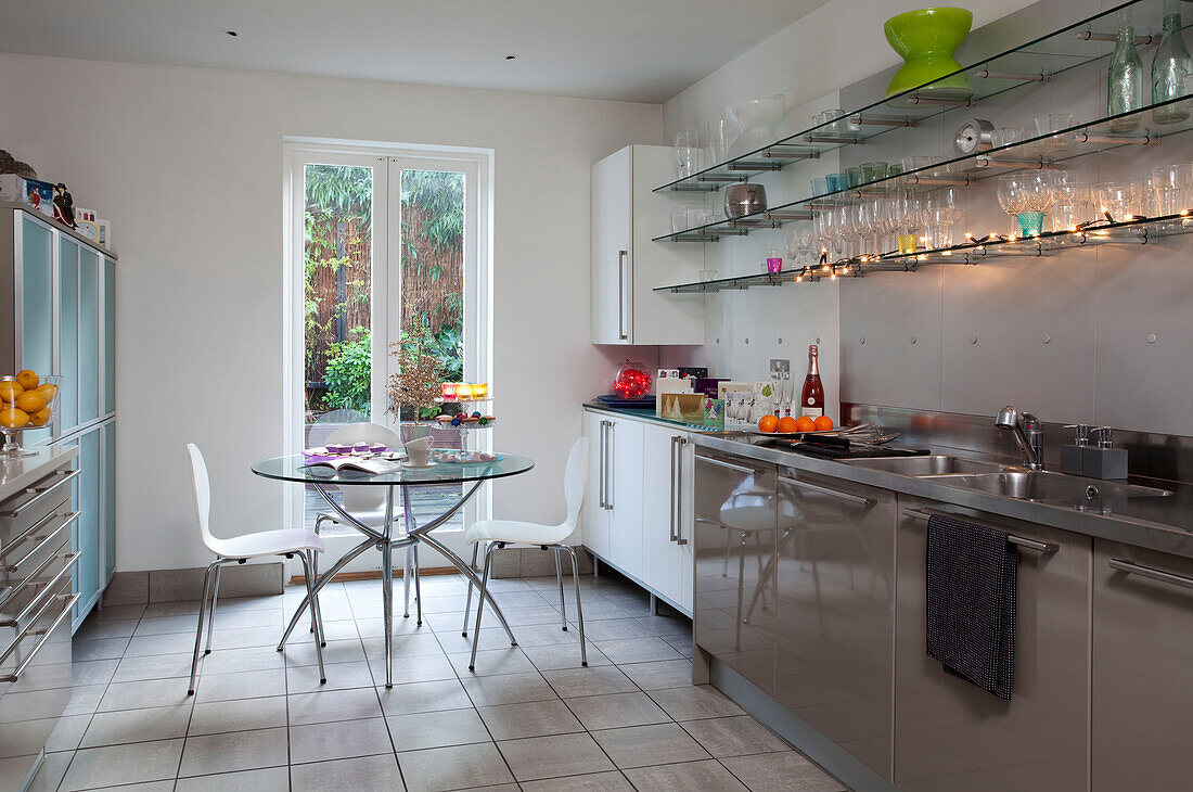 Glass table in contemporary London kitchen with fairlights and variety of cupboard units, UK