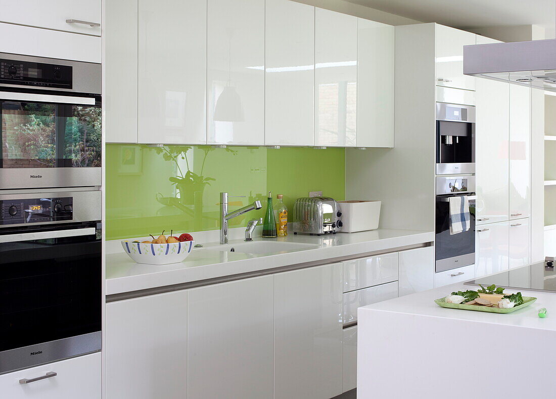 Weiße Einbauküche mit grüner Spritzschutzwand und integrierten Geräten in einem modernen Haus in London, England, UK