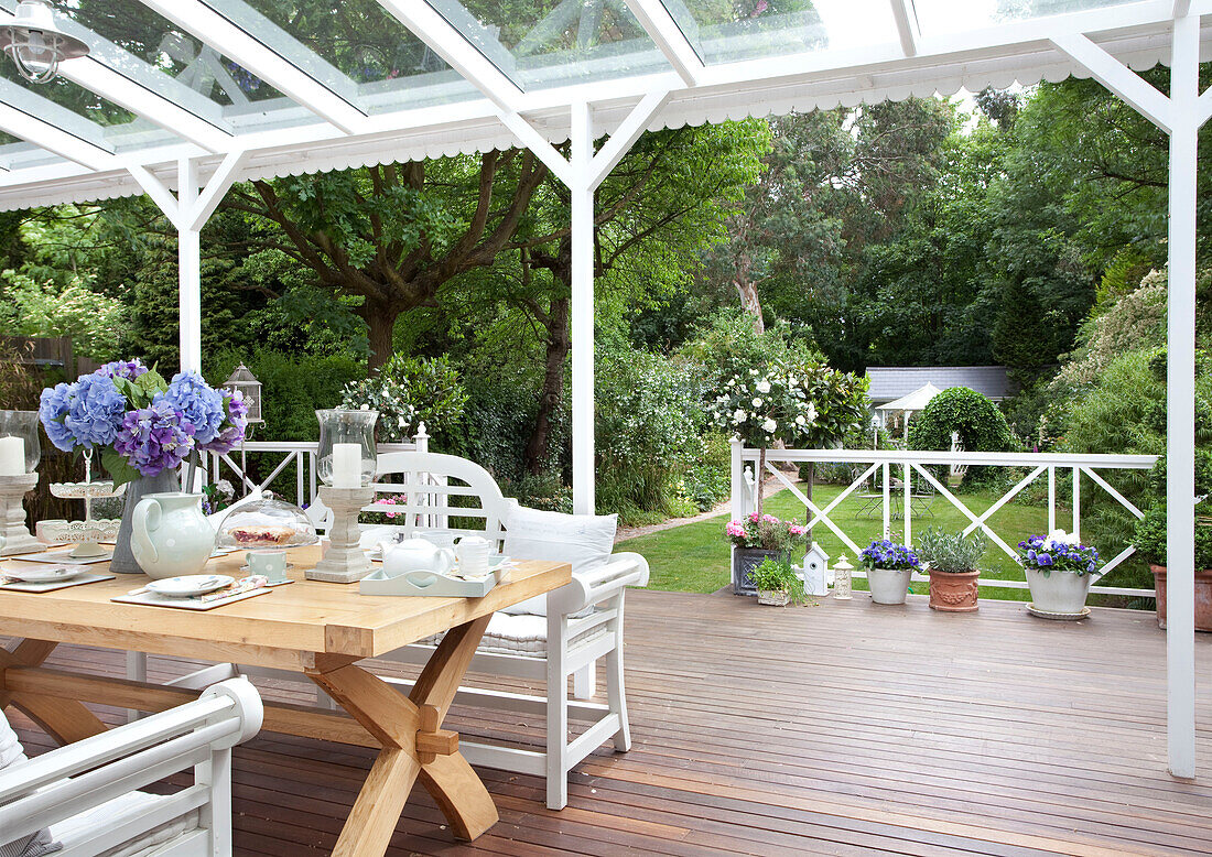 Painted bench seats at wooden table on covered wooden terrace of London home, UK