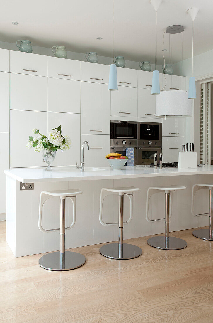 Barhocker an der Frühstücksbar in einer weißen Einbauküche in einem modernen Londoner Haus, UK