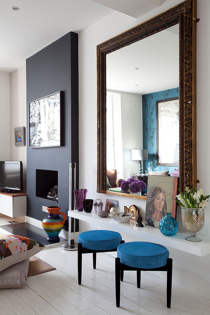 Blaue Hocker an einem Regal mit großem Spiegel, der den Raum in einem modernen Haus in London reflektiert, UK