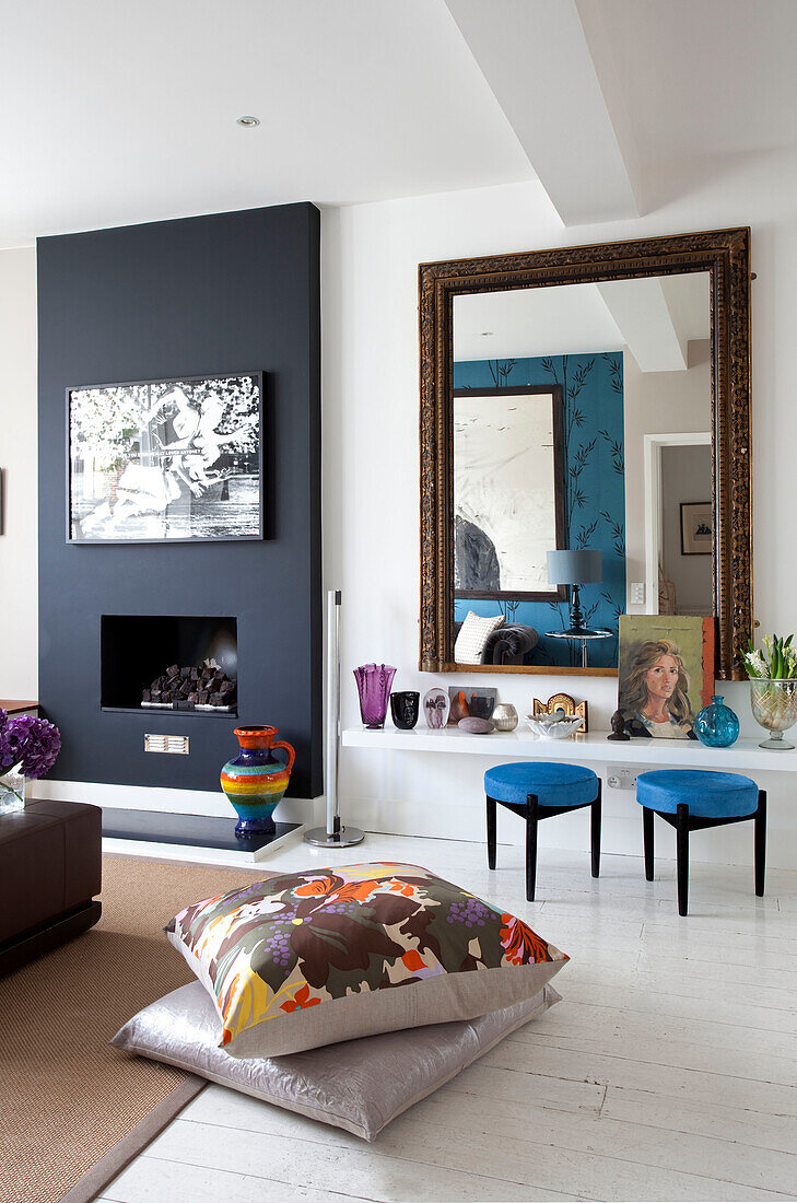 Black chimney breast and mirror reflecting living room with floor cushions in contemporary London home, UK
