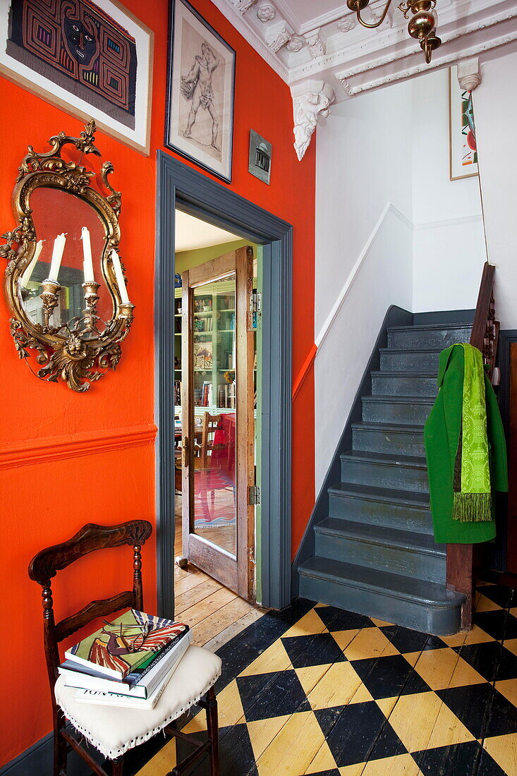 Artwork and mirror in orange hallway with grey painted stairs in London home England UK