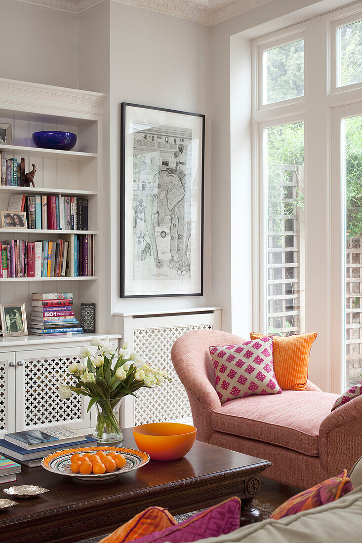 Cut tulips and satsumas on wooden coffee table with bookshelves and double arm chaise in contemporary London family home, UK