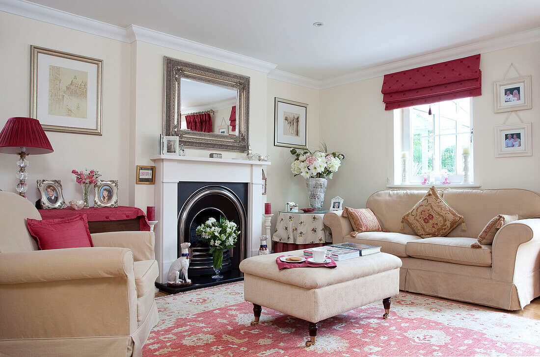 Cream three-piece suite with ottoman and red furnishings in living room of Kent cottage, England, UK