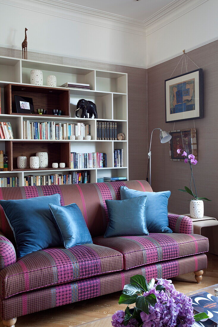 Blaue Kissen auf Sofa mit Bücherregal im Wohnzimmer eines modernen Londoner Stadthauses, England, Vereinigtes Königreich