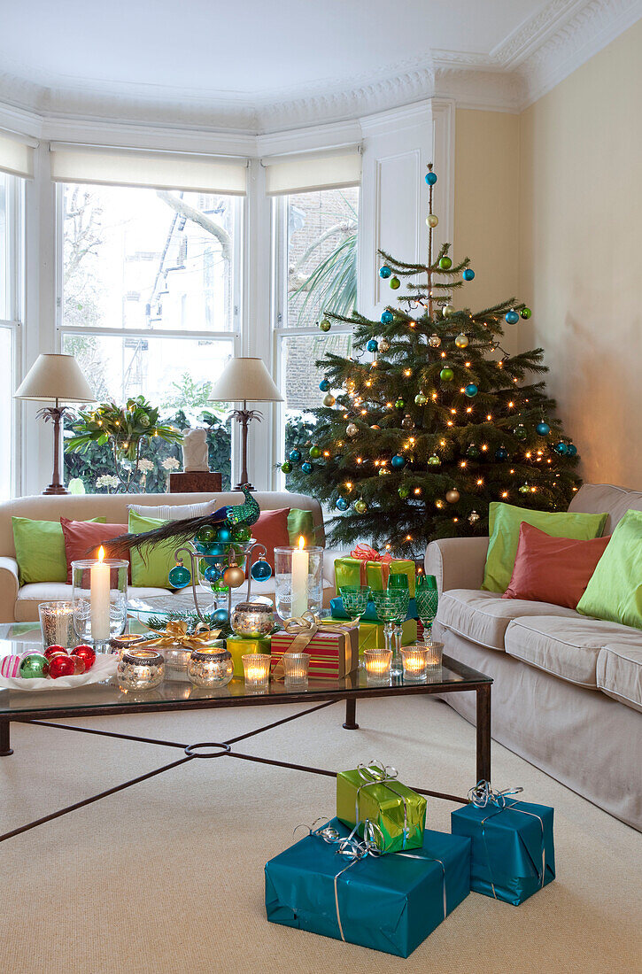 Lit candles and Christmas presents with tree in London living room, UK