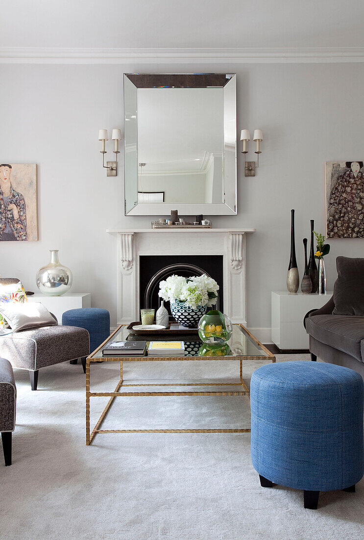 Couchtisch mit Glasplatte und Spiegel mit blauen Hockern im Wohnzimmer einer Londoner Wohnung, UK