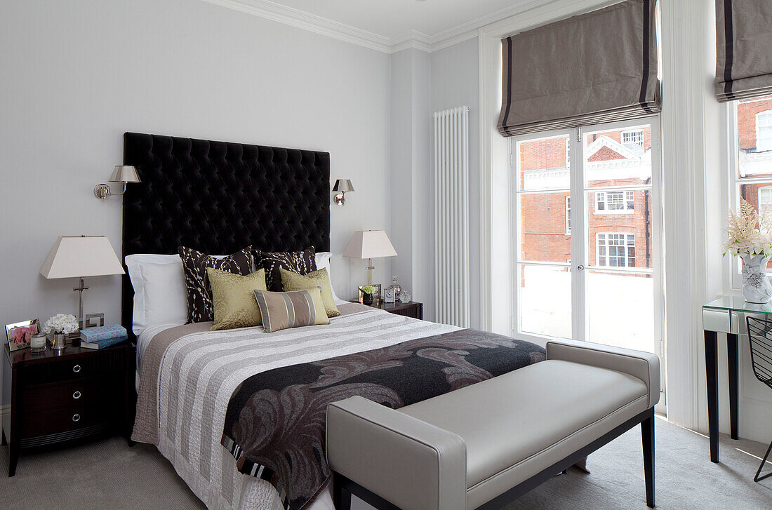 Blattgemusterte Decke auf Doppelbett mit schwarzem, geknöpftem Kopfteil im Schlafzimmer einer Londoner Wohnung, UK