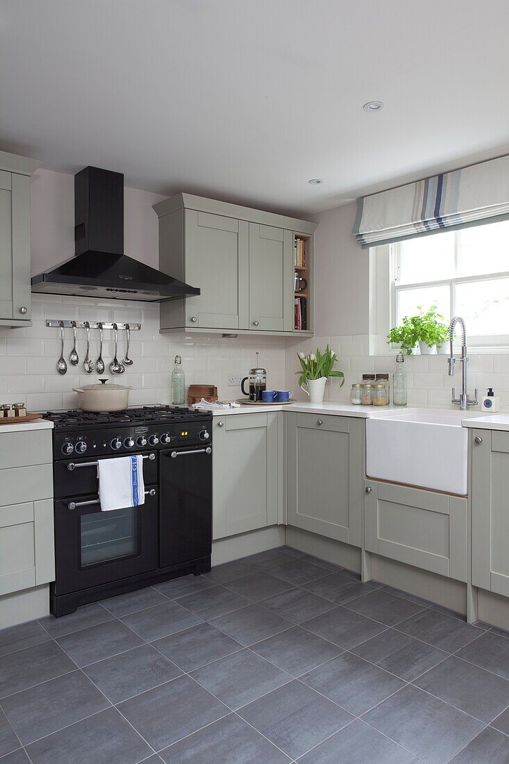 Pastel green fitted kitchen with butler sink and black range oven in contemporary London townhouse, England, UK