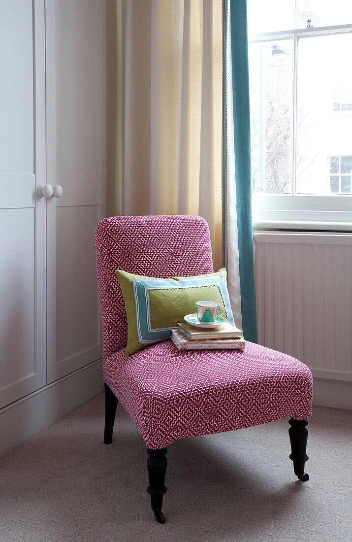 Teacup and books with applique cushion on upholstered chair in London bedroom, England, UK