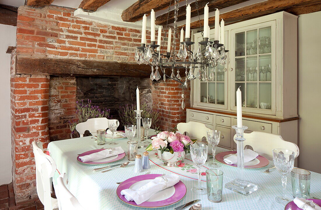 Dining table with glass chandelier and exposed brick fireplace in Maidstone farmhouse, Kent, England, UK
