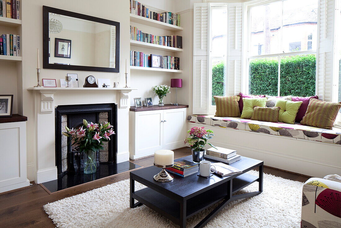 Recessed bookshelves with Victorian fireplace in living room with upholstered window seat in London townhouse, England, UK