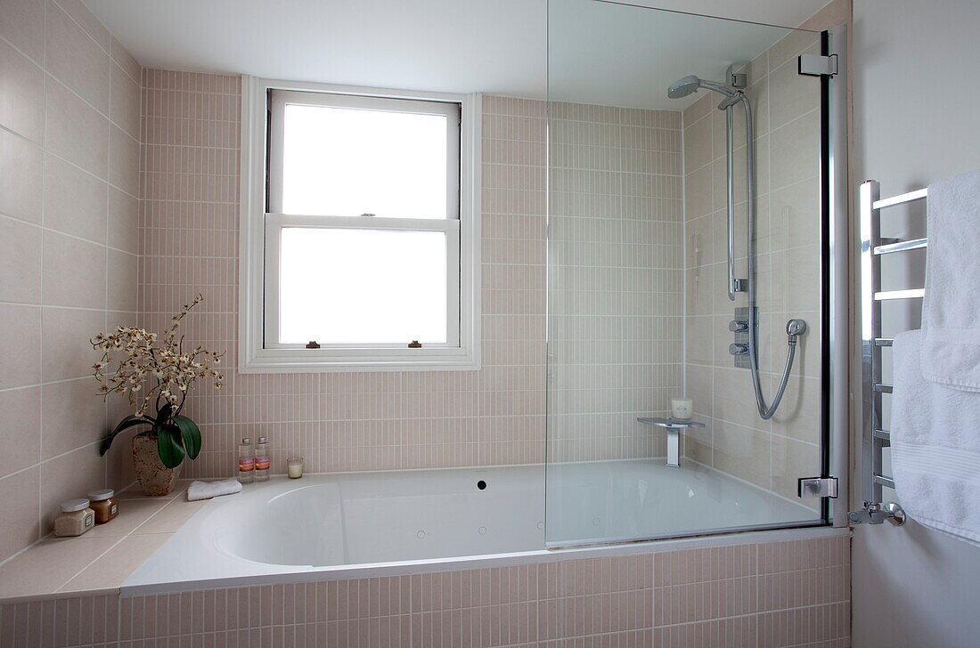 Pastellrosa geflieste Badewanne mit Duschabtrennung in einem modernen Londoner Stadthaus, England, UK