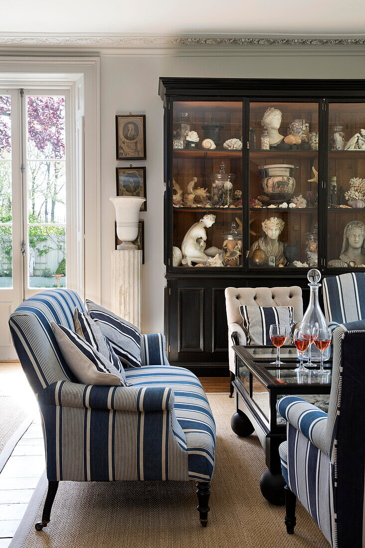 Blue and white sofa and display cabinet with historic artefacts in drawing room of Sussex country home England UK