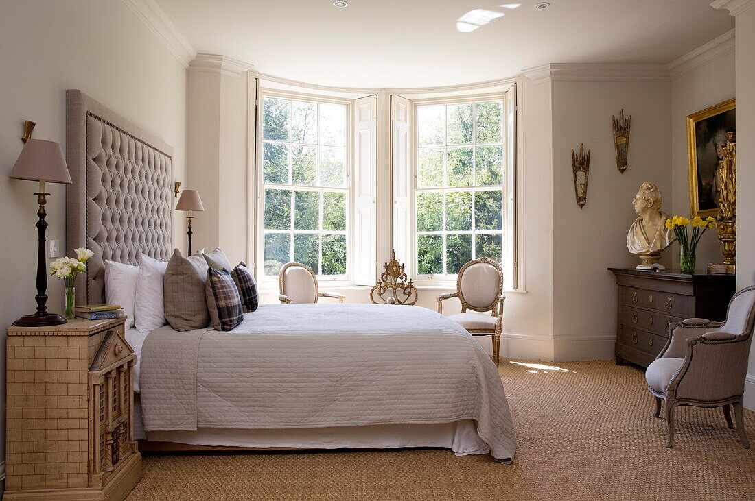 Sonnendurchflutetes Schlafzimmer mit großem gepolsterten Kopfteil und Naturfaserteppich in einem Landhaus in Sussex England UK