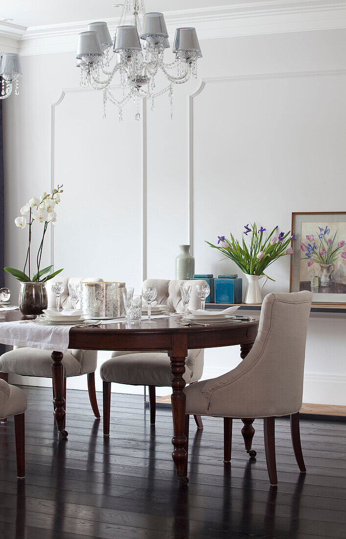 White dining chairs and cut glass chandeliers in dining room of contemporary Surrey country home England UK