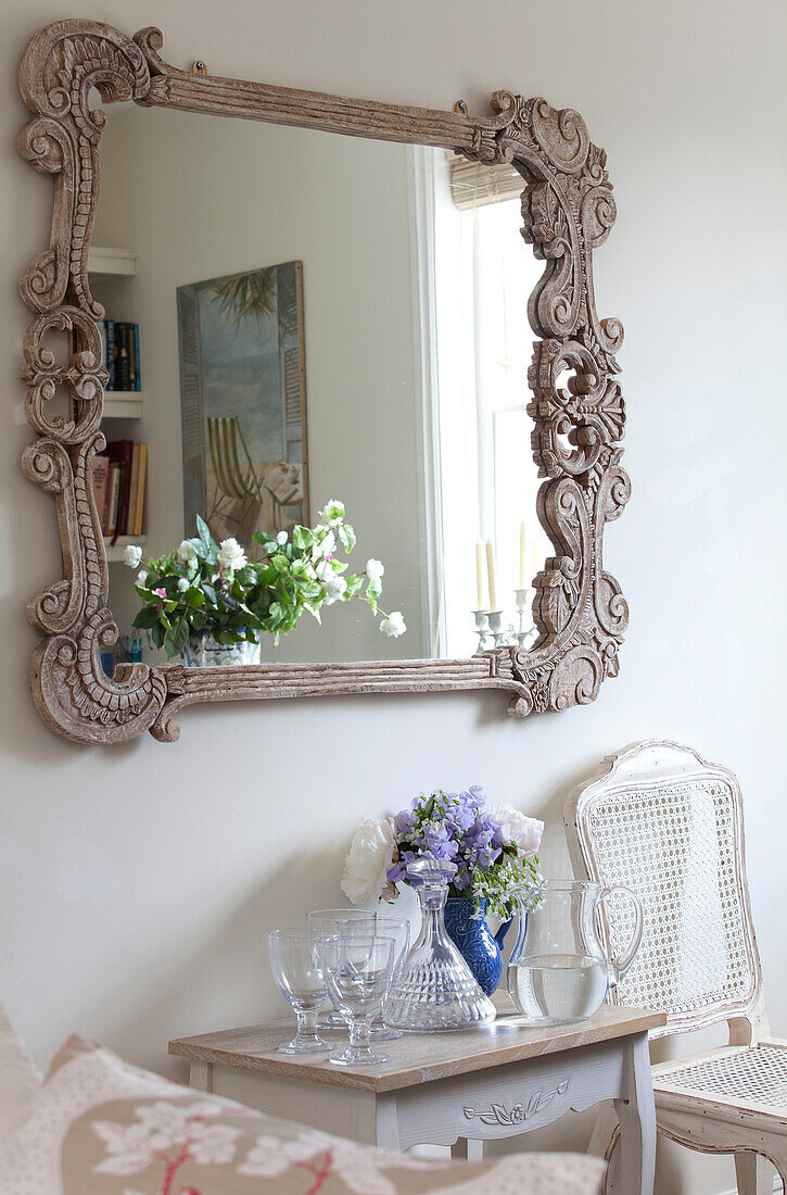 Ornate carved mirror reflecting flower arrangement in living room of coastal Sussex cottage, England, UK