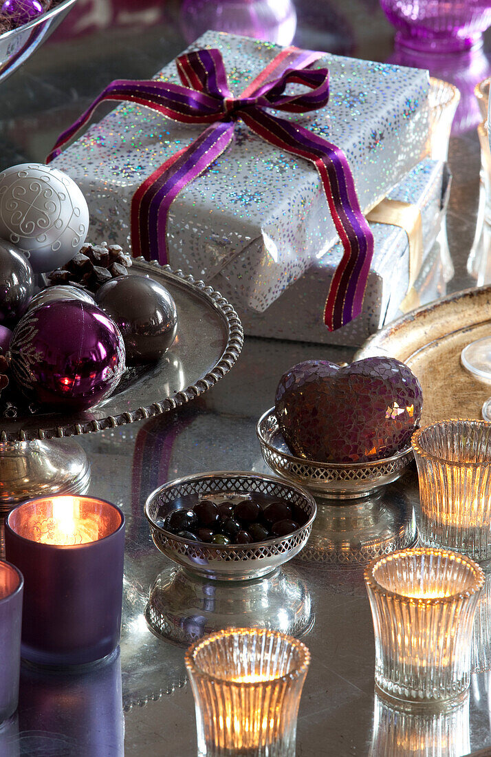 In Geschenkpapier verpackte Geschenke und Weihnachtskugeln in einem Bauernhaus in Surrey mit Teelichtern, England, UK