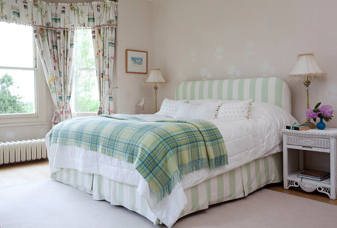 Grüne Schottenkaro-Decke auf einem Doppelbett mit gestreiftem Kopfteil und Volant in einem Landhaus in Sussex, England, UK