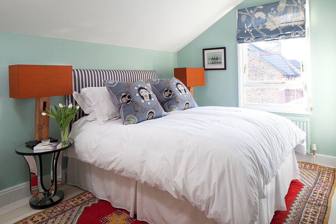 Doppelbett mit bedruckten Kissen in einem mintgrünen Zimmer in einem Haus in London, England, UK