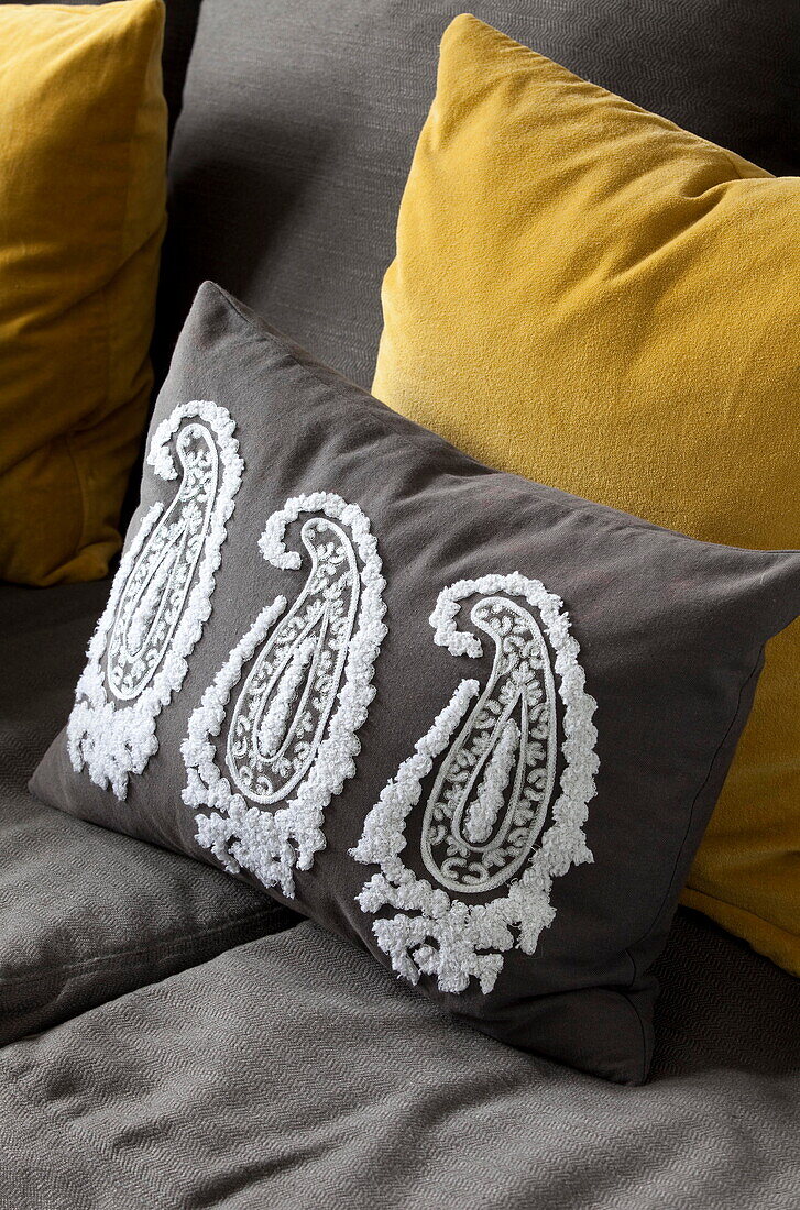 Paisley motif and yellow cushions on grey sofa in London townhouse England UK