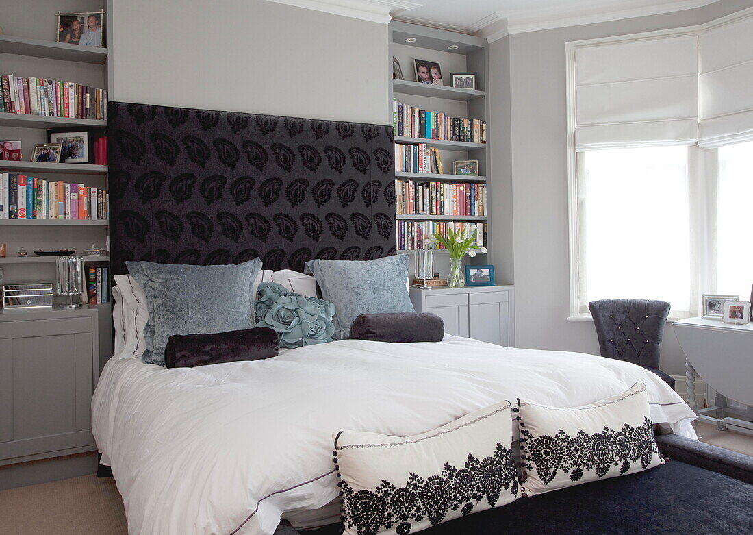 Doppelbett mit gemustertem Kopfteil und Bücherregalen in einem Londoner Stadthaus England UK