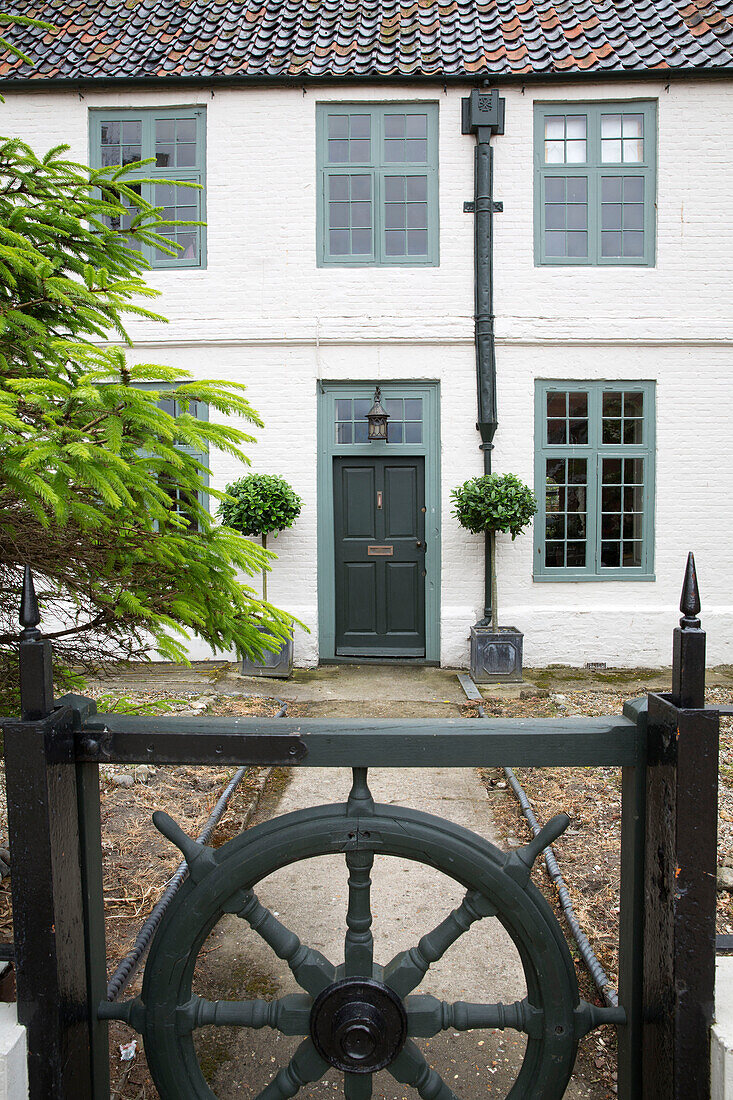 Ships wheel gate at entrance to whitewashed coach house facade in Wells next the Sea, Norfolk, England, UK