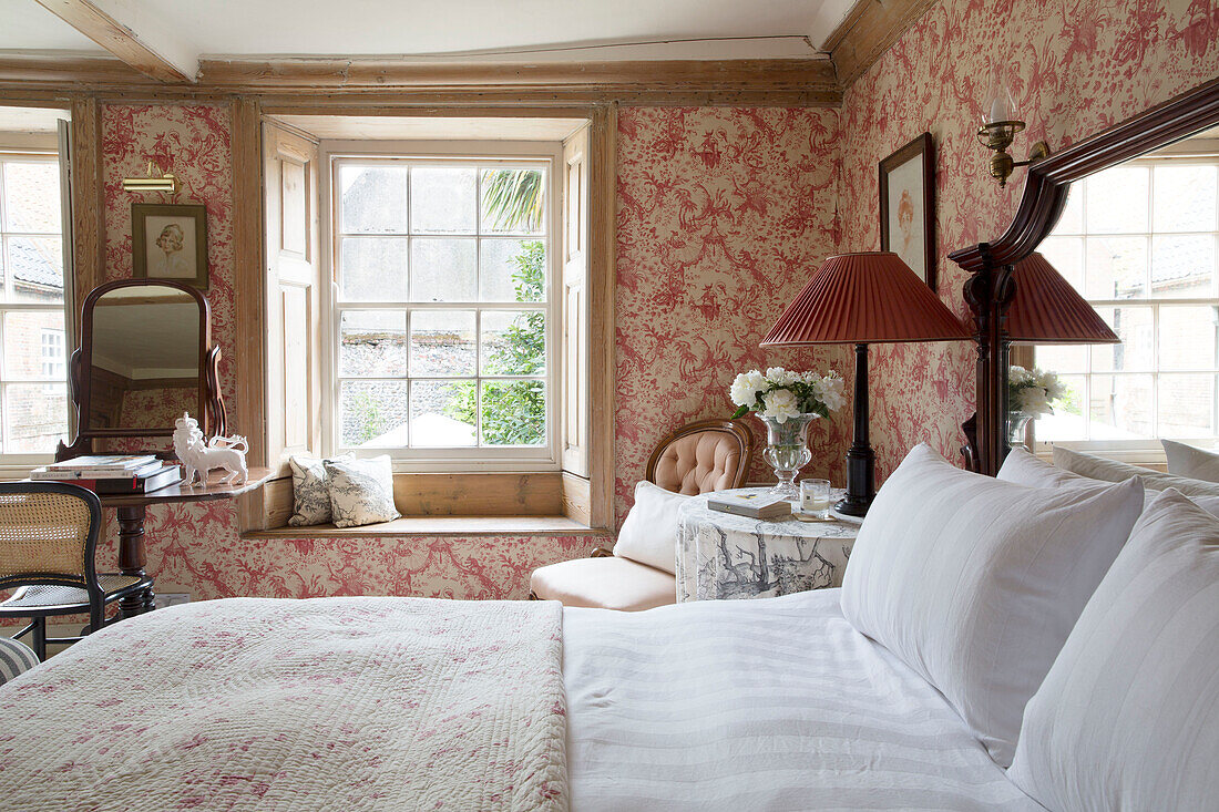 Red lamp at bedside in floral patterned room with window seat in Wells next the Sea home, Norfolk, England, UK