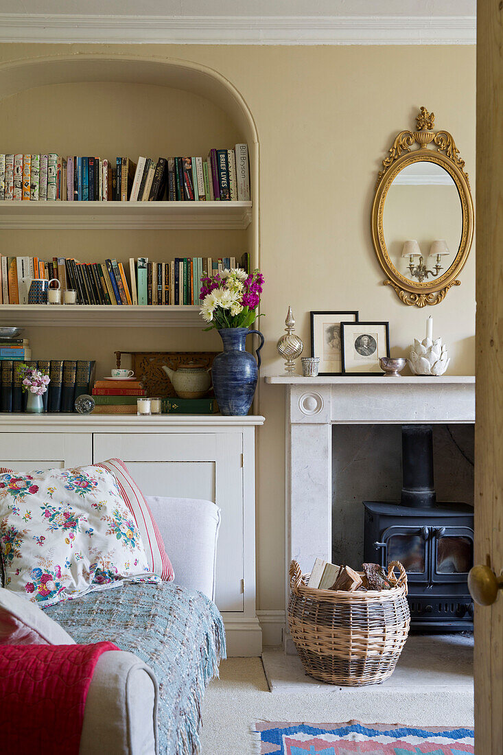 Log basket at fireside with recessed bookshelves in Dorset cottage interior, England, UK