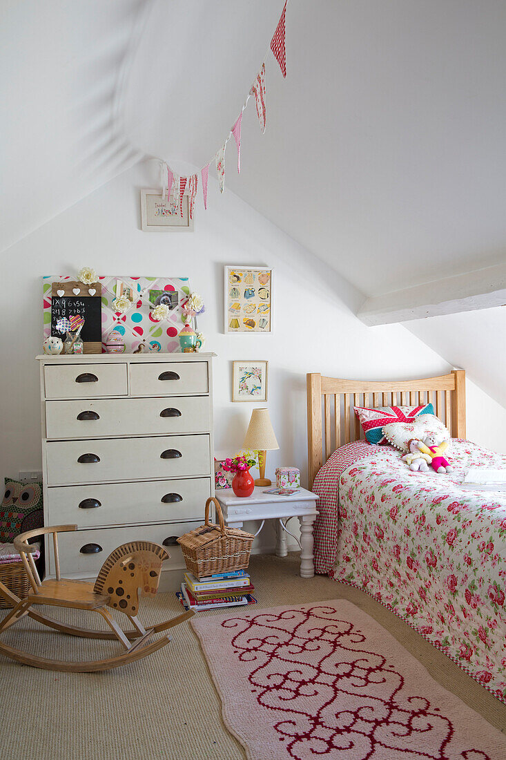 Bettdecke mit Rosenmuster und Wimpel im Schlafzimmer eines Mädchens im Dachgeschoss eines Cottage in Dorset, England, UK