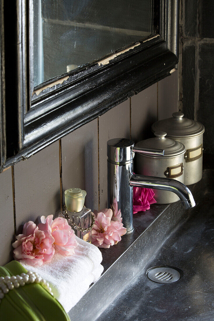 Chipped black mirror frame above chrome tap on washbasin in Brittany cottage Western France