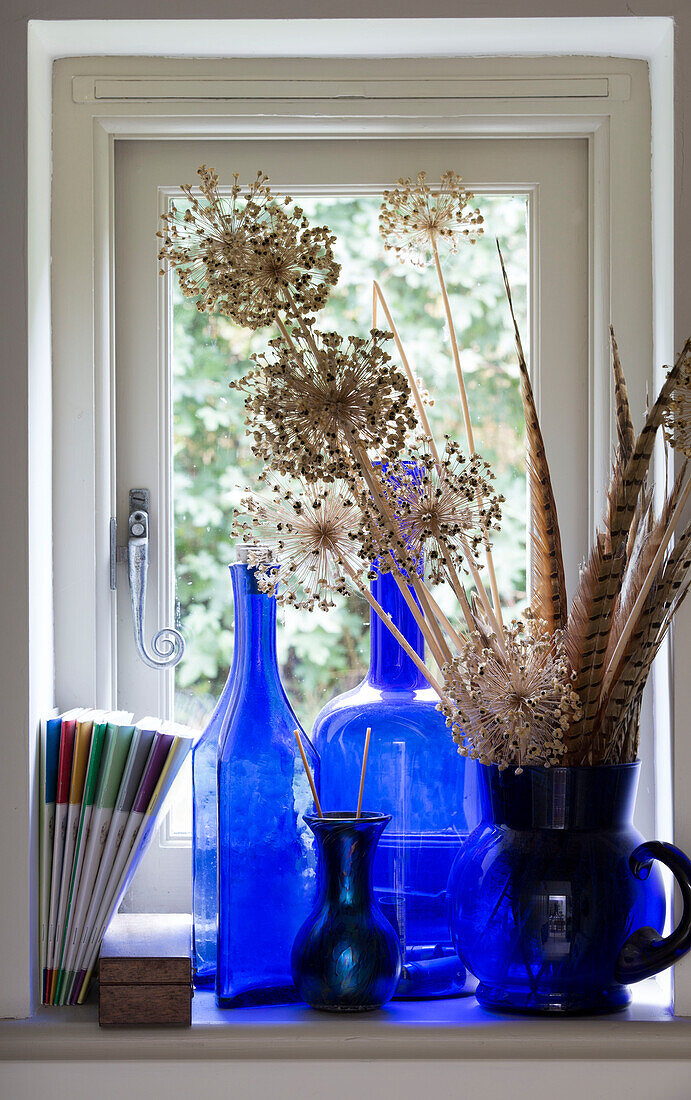Blaue Glaswaren mit Federn und getrockneten Blumen auf der Fensterbank in einem Haus in Sussex Downs, England UK