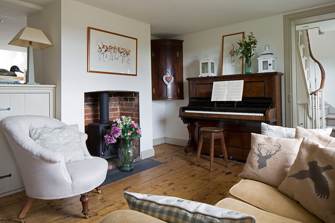 Holzklavier und weißer Sessel im Wohnzimmer eines Hauses in den Sussex Downs, England, Vereinigtes Königreich